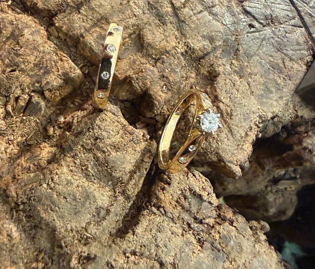 A solitaire-style ring and coordinating stone-set band, photographed on textured bark